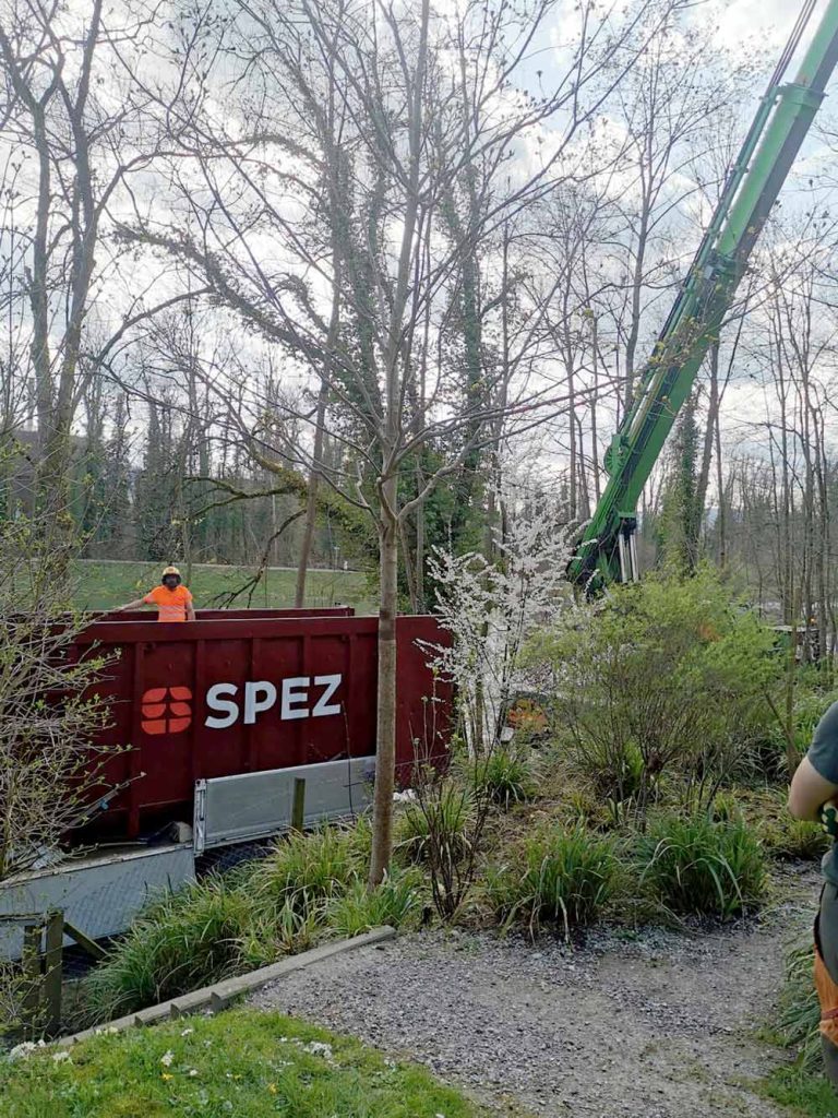 Ein Lastwagenkran der Firma SPEZ transportiert Material in einem bewaldeten Gebiet.