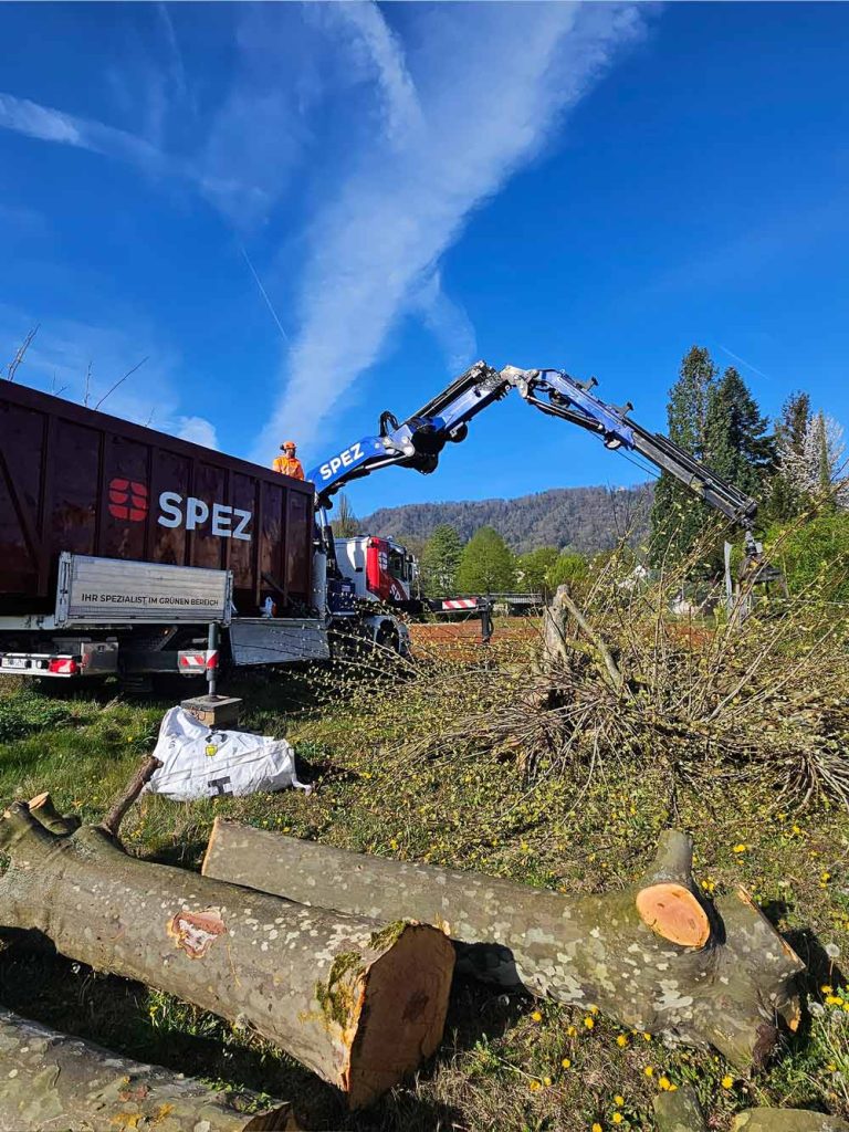 Ein Lastwagenkran der Firma SPEZ hebt Baumaterialien in einem offenen Feld an einem sonnigen Tag.